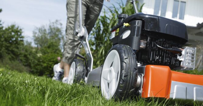 Person pushing a lawnmower across a grassy area.