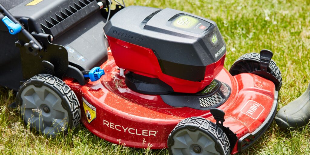 Close-up of a red Toro Flex Force 22-inch Recycler electric battery lawn mower on a green lawn. The mower has a black chassis, yellow highlights, and white text.