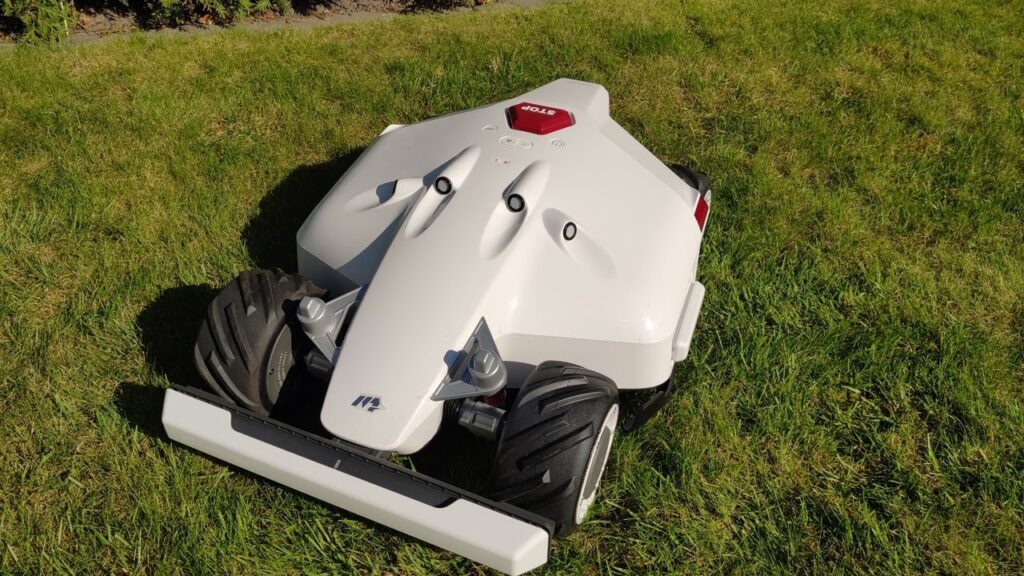 A black robotic lawn mower with green detailing sits on a lush green lawn. The text "Mammotion Luba AWD 5000 Robot Lawn Mower" is written on the side of the mower.